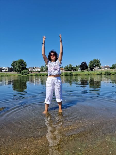 Tatjana Fast praktiziert Qigong im See mit erhobenen Armen unter freiem Himmel.