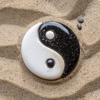 Yin-Yang-Symbol aus schwarzen und weißen Steinen im Sand.